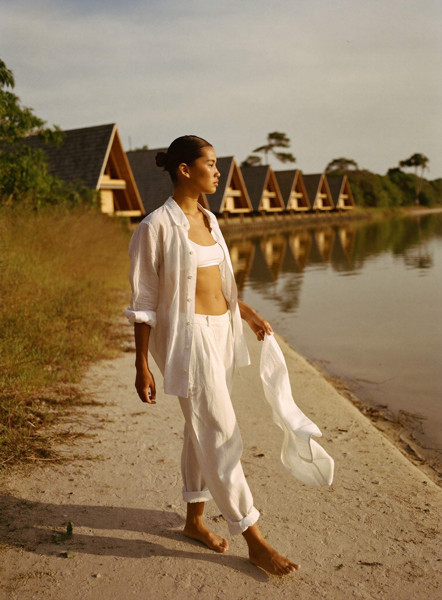 Mulher de branco caminhando em frente à fileira de chalés A-frame no lago